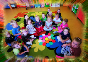 Grupa dzieci siedzi na dywanie, przed nimi leżą kolorowe koła.